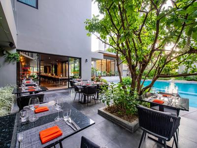 Area esterna moderna dell'hotel con tavoli, sedie, un albero e una piscina.