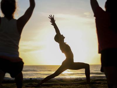 Silhouetten von Menschen, die Yoga am Strand bei Sonnenuntergang praktizieren.