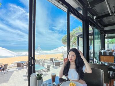 Frau sitzt an einem Tisch mit Frühstück und Blick auf Außenterrasse und Meer
