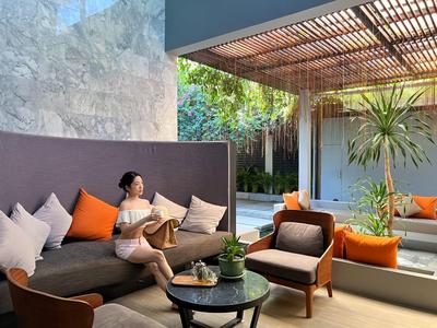 Frau entspannt sich mit Buch auf graßer Couch im modernen Außenbereich mit Pflanzen.