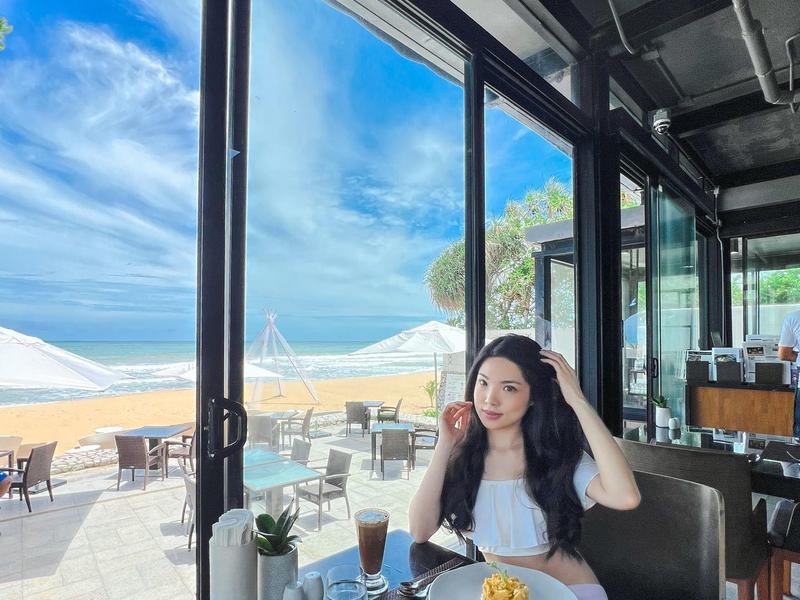 Frau sitzt an einem Tisch mit Frühstück und Blick auf Außenterrasse und Meer