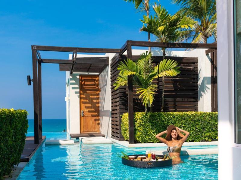 Frau entspannt im Pool einer modernen Villa mit Blick auf das Meer und blauem Himmel.