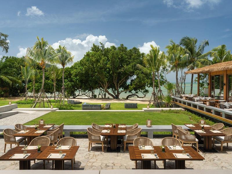 Area esterna di un hotel con tavoli e sedie con vista su un giardino curato e palme.