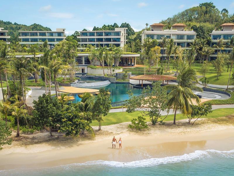 Vista di una spiaggia con palme, piscina e ville moderne su una collina.