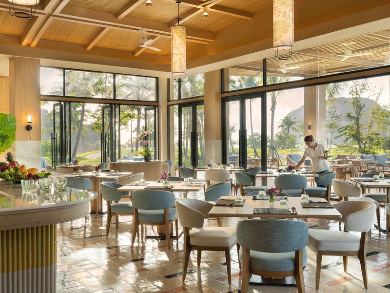 Ristorante luminoso con sedie moderne, tavoli e grandi finestre con vista sugli alberi.