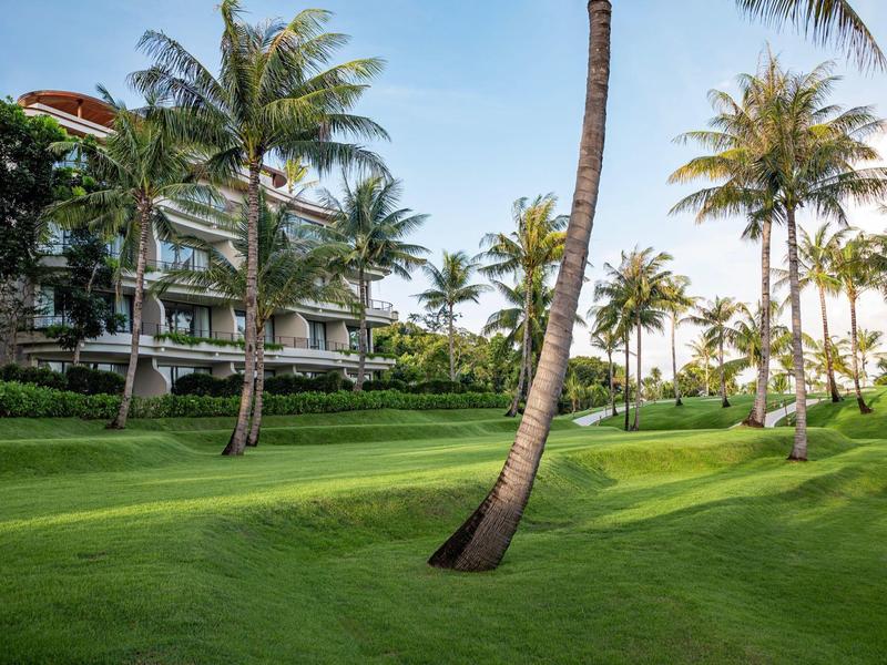 Giardino verde con palme davanti a un edificio alberghiero in una giornata di sole.