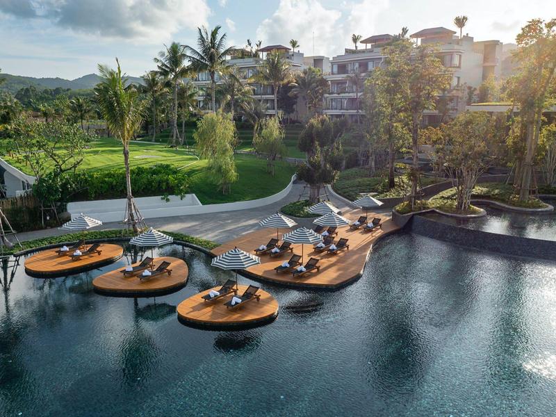 Piattaforme in legno galleggianti con posti a sedere su una piscina accanto a un hotel tropicale.