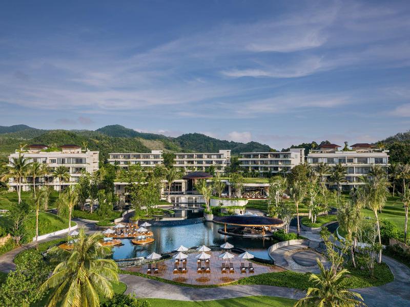 Resort di lusso con più edifici, grande piscina e giardino tropicale sotto un cielo azzurro.