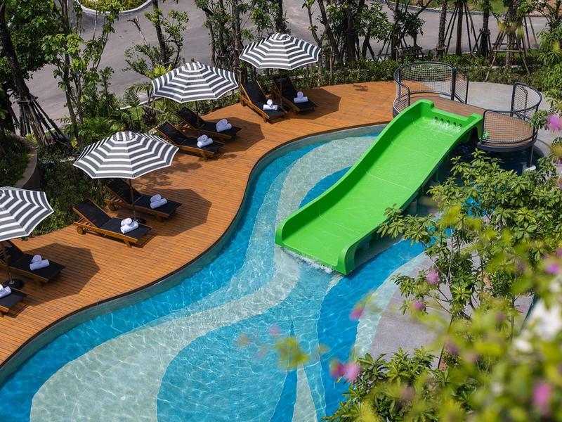 Area piscina con scivolo verde, lettini e ombrelloni a righe bianche e nere