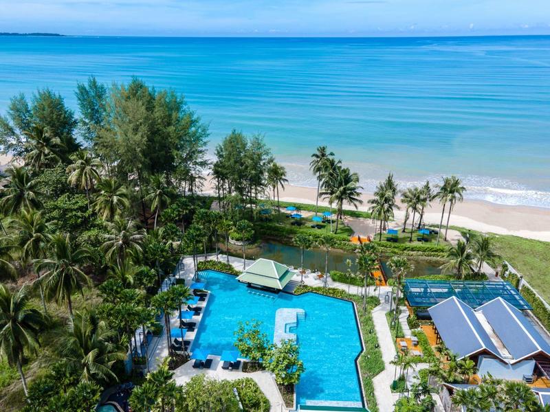 Pohled na bazén obklopený palmami a pláží u tyrkysového moře.