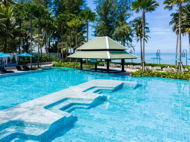 Velký bazén s deštníky a palmami na pláži pod jasnou oblohou