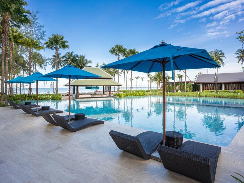 Moderní bazénová zóna s modrými slunečníky a lehátky v tropickém hotelu.