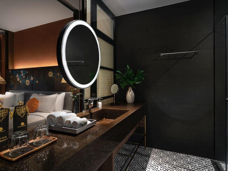 Moderní hotelové umyvadlo s kulatým osvětleným zrcadlem a luxusním zařízením.