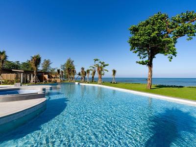 Velký bazén s průzračně modrou vodou, palmami a trávou pod modrou oblohou.