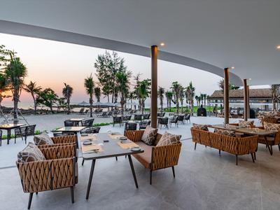 Otevřený hotelový prostor se sezením a výhledem na palmy a západ slunce na pláži.