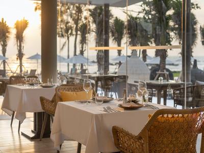 Elegantní restaurace s prostřenými stoly a výhledem na pláž při západu slunce.