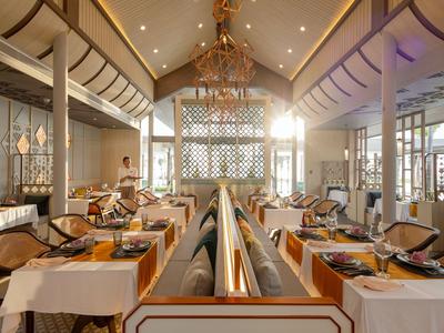 Světla restaurace s elegantními bílými stoly a dekorativními dřevěnými panely pod vysokými klenutými stropy.