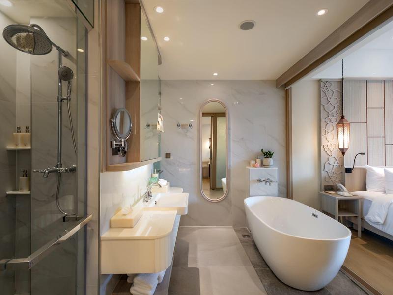 Moderní koupelna s volně stojící vanou, dvojumyvadly a sprchovým koutem v hotelovém pokoji.