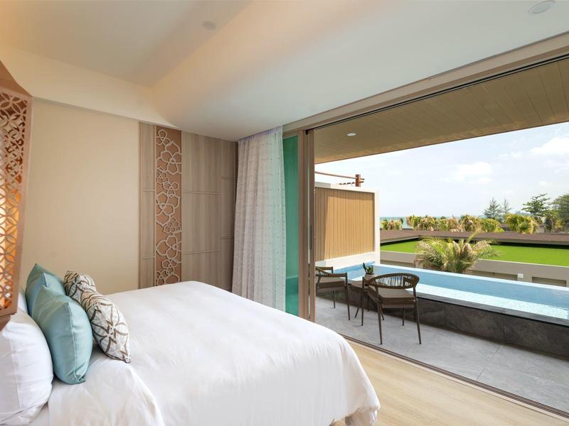 Světlo ložnice s velkou postelí, dveřmi na balkón a výhledem na bazén a zahradu.