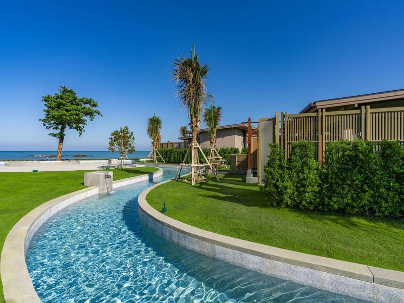 Rezortní oblast s klikatým bazénem, palmami a modrou oblohou u moře.