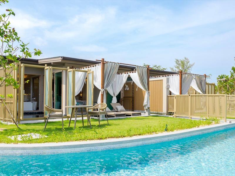 Moderní rekreační bungalovy s velkými okny a odpočinkovými zónami u průzračného bazénu.