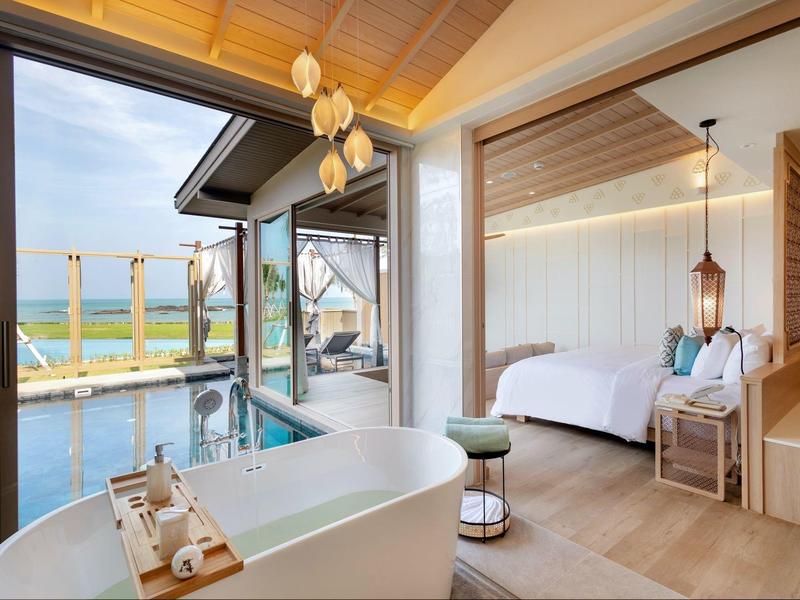 Moderní hotelový pokoj s volně stojící vanou s výhledem na bazén a moře.