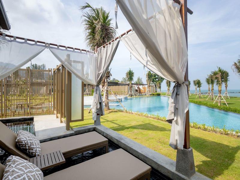 Pohodlná lehátka pod altánem s výhledem na bazén a zelený trávník.