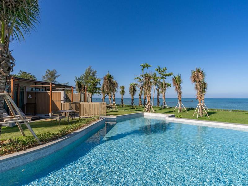 Moderní bazén s čistou modrou vodou, obklopený palmami s výhledem na moře.