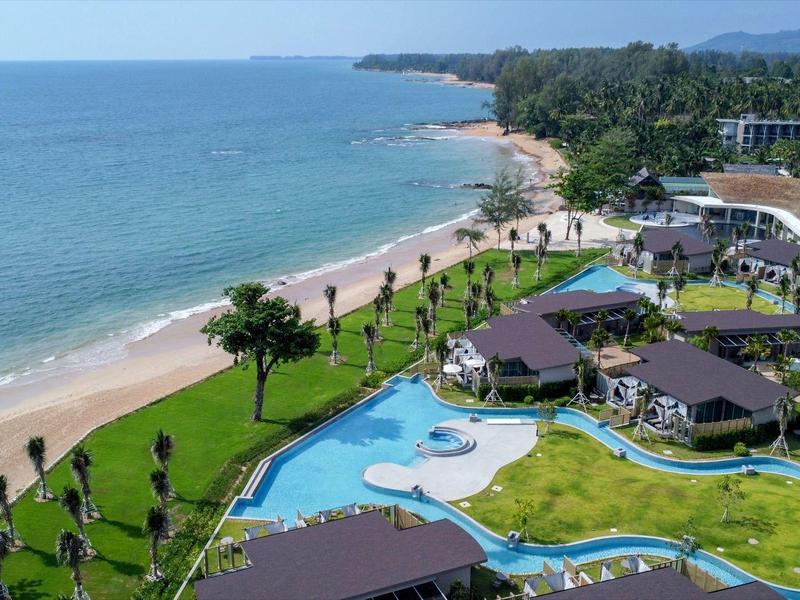 Pohled na tropické plážové letovisko s bazénem, palmami a písečnou pláží u moře.