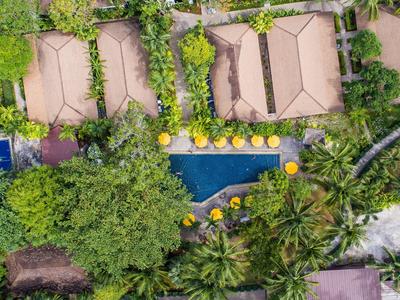 Vista aerea di un resort con piscina circondato da alberi e ombrelloni gialli.