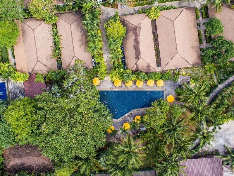 Vista aerea di un resort con piscina circondato da alberi e ombrelloni gialli.