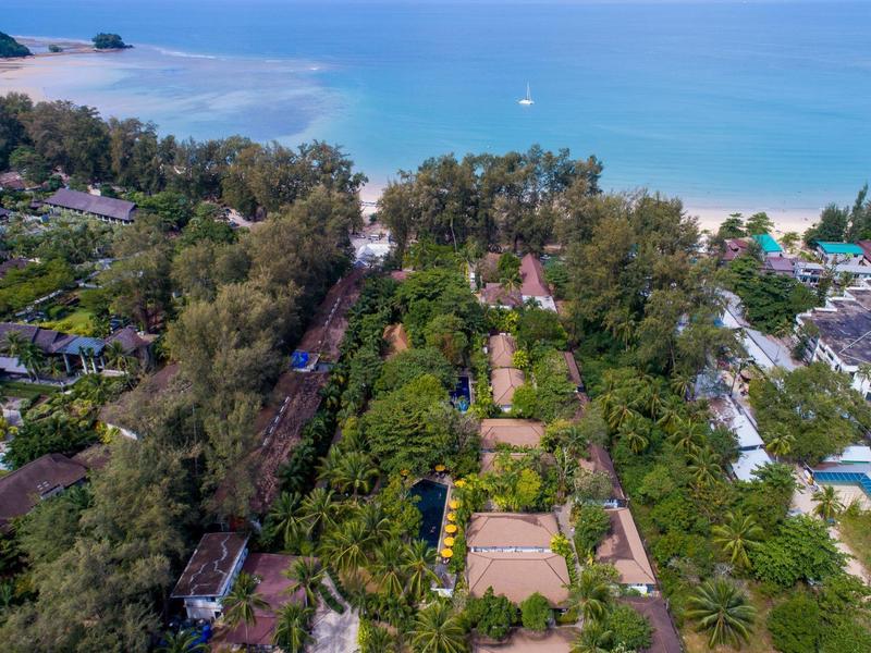 Vista aerea di un hotel circondato da verde rigoglioso con il mare blu sullo sfondo.
