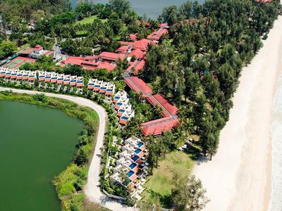 Luxuriöse Ferienanlage mit roten Dächern zwischen grünem Wald, See und weißem Sandstrand am Meer.