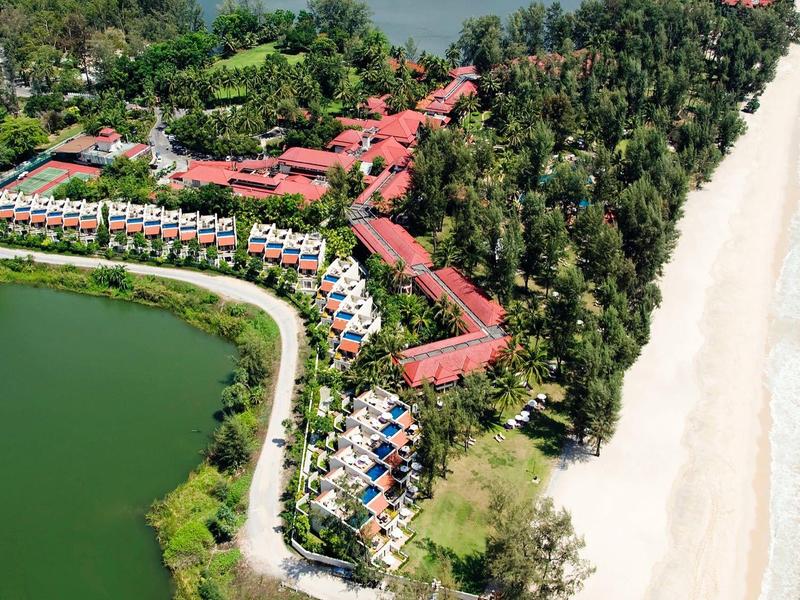 Luxuriöse Ferienanlage mit roten Dächern zwischen grünem Wald, See und weißem Sandstrand am Meer.