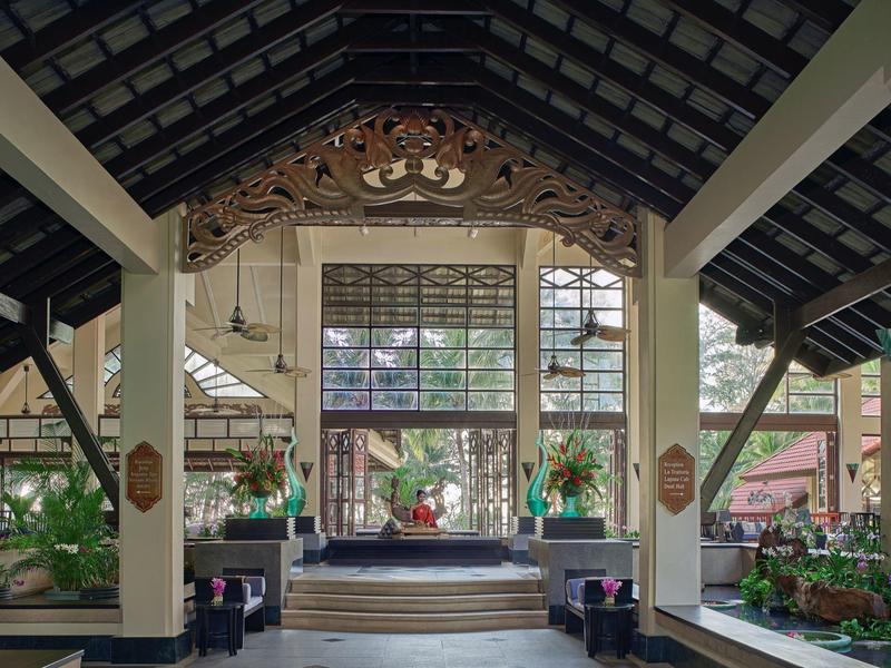 Großes, offenes Holzdach mit verzierten Balken über einer Bühne und vielen Pflanzen im Warmen Licht.