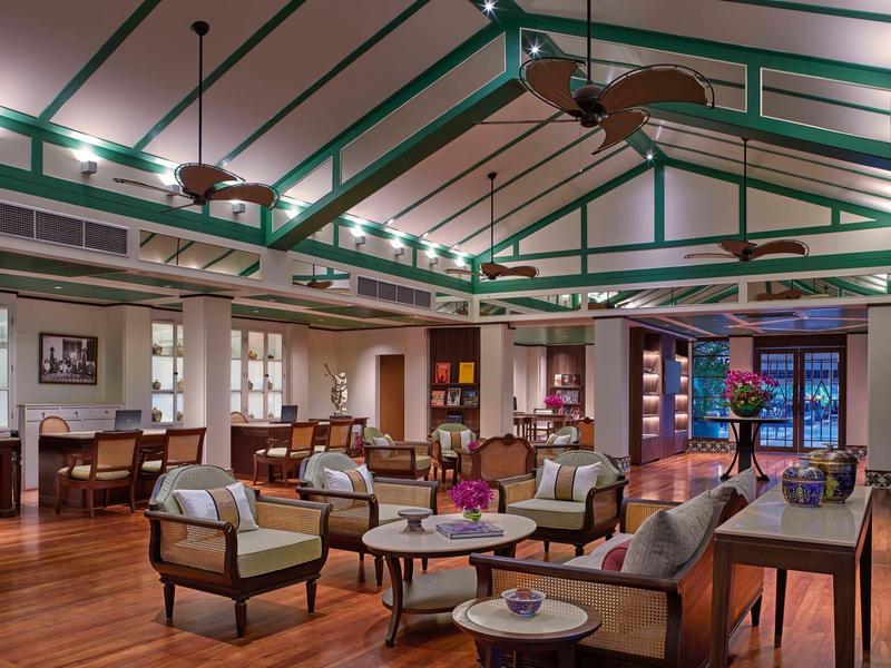 Großer Raum mit Holzfußboden, hohen Decken, Sesseln, Sofas und runden Tischen in warme Farbtönen.