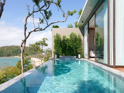 Infinity pool overlooking the sea and green hills beside a modern glass villa