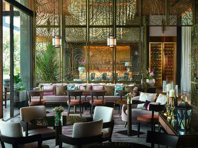 Elegantes Wohnzimmer mit großen Fenstern, Holzmöbeln, Pflanzen und warmem Licht, gemütliche Atmosphäre.