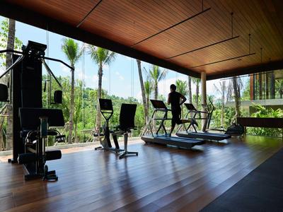 Modern gym with equipment and large windows overlooking palm trees and garden.