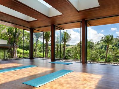 Bright yoga studio with wooden floor and panoramic windows overlooking tropical plants.