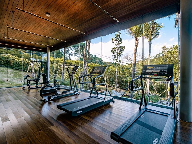 Moderne Fitnessstudio mit Holzboden, Laufbändern und großen Glasfenstern mit Blick ins Grüne.