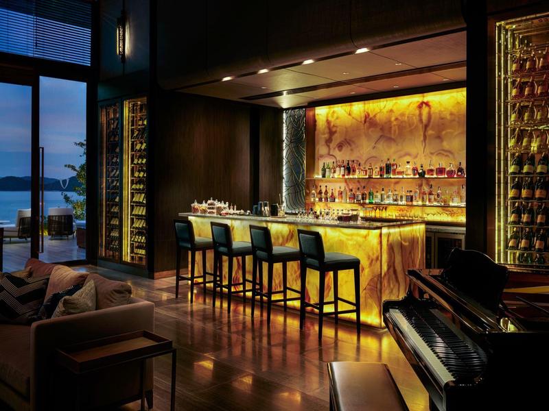 Elegante Bar mit warmem Licht, moderner Einrichtung, Ledersesseln und Blick auf das Meer bei Dämmerung.