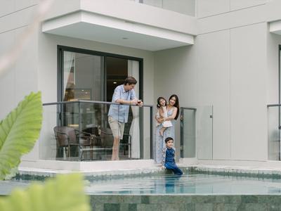 Familie mit zwei Kindern spielt an einem Pool vor einem modernen Haus mit Glasgeländer.