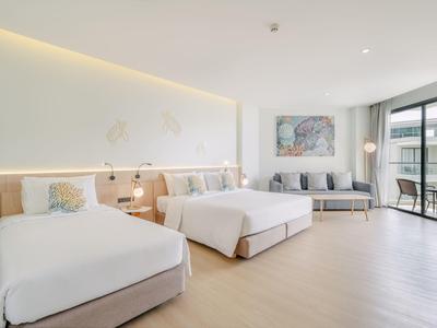 Modernes Hotelzimmer mit zwei Doppelbetten, Sofa und großem Fenster mit Balkonblick.