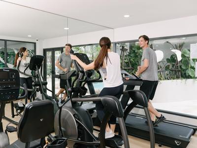 Menschen trainieren gemeinsam auf Laufbändern in einem modernen Fitnessraum mit Spiegeln und großen Fenstern.