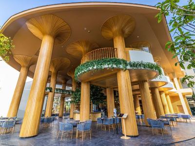 Außenbereich eines Restaurants mit dicken, goldfarbenen Säulen und blauen Sitzgelegenheiten unter einem gewölbten Dach.