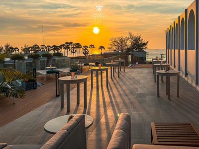 Terrasse mit Tischen und Stühlen bei Sonnenuntergang mit Meerblick und Palmen.