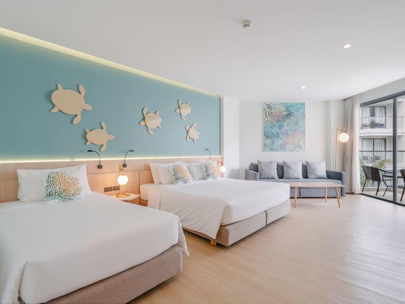 Modernes Hotelzimmer mit zwei Doppelbetten, Sitzbereich und Balkon mit Glasfront.