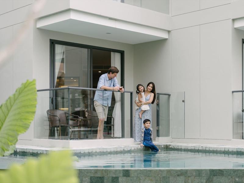 Familie mit zwei Kindern spielt an einem Pool vor einem modernen Haus mit Glasgeländer.