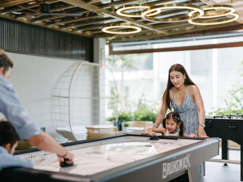 Familie spielt Airhockey in einem modernen Indoor-Freizeitbereich mit Sofa und dekorativer Beleuchtung.